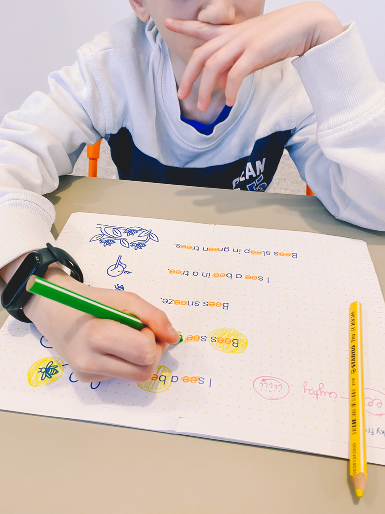 Na zdjęciu chłopiec uczy się rozpoznawać dźwięki w języku angielskim. Zaznacza litery kolorowym pisakiem